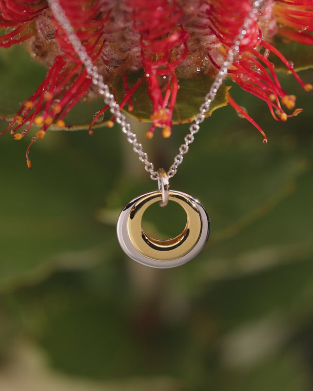 Video of ENVYONE 18K Gold-Plated two-tone pendant necklace featuring polished gold and silver concentric rings styled among red flowers.