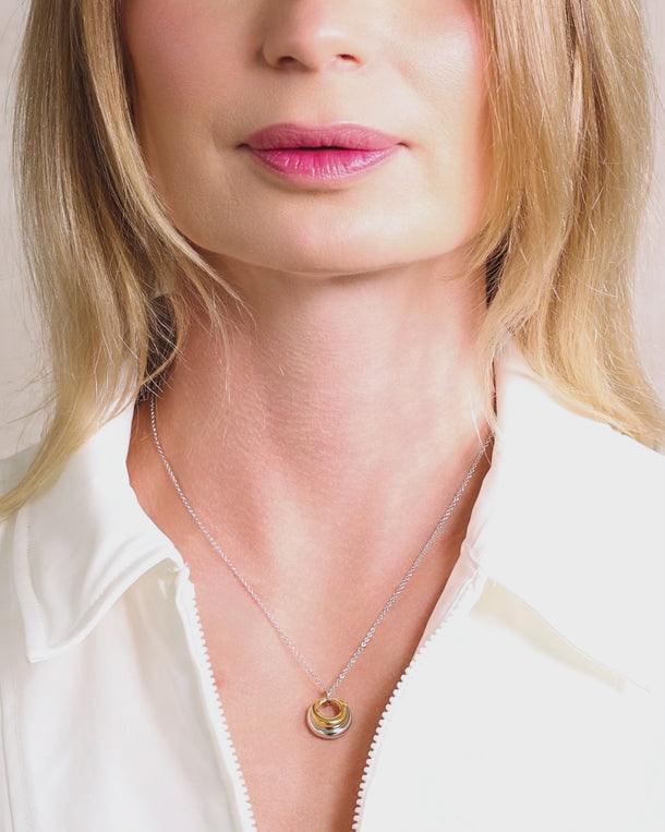 Video of woman wearing an ENVYONE two-tone pendant necklace featuring layered gold and silver concentric rings on a delicate silver-tone chain.