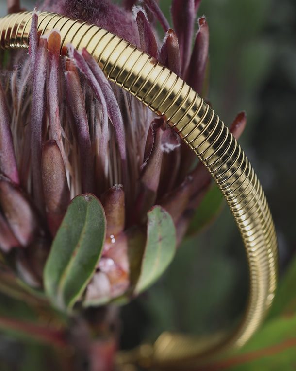Closeup of an ENVYONE 18K Gold Plated stainless steel collar necklace styled across a sculptural botanical flower.