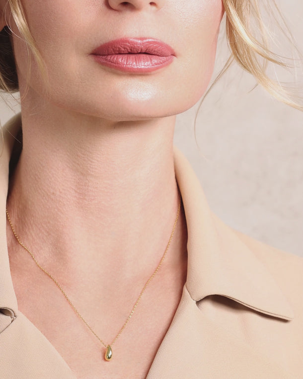 Closeup video of a woman wearing an ENVYONE 18K Gold Plated 925 Sterling Silver necklace with a polished teardrop pendant.