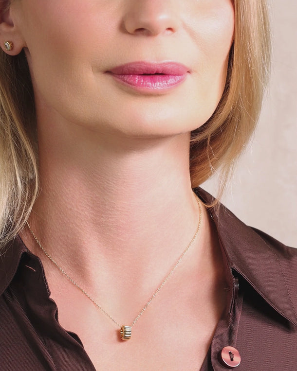Closeup video of a woman wearing an ENVYONE 18K Gold-Plated PVD necklace with a polished ribbed gold pendant.